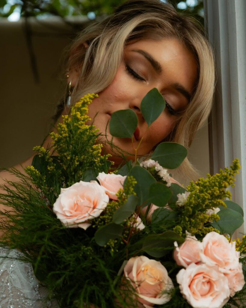 Woman with closed eyes holds peach roses and greenery bouquet close to her face