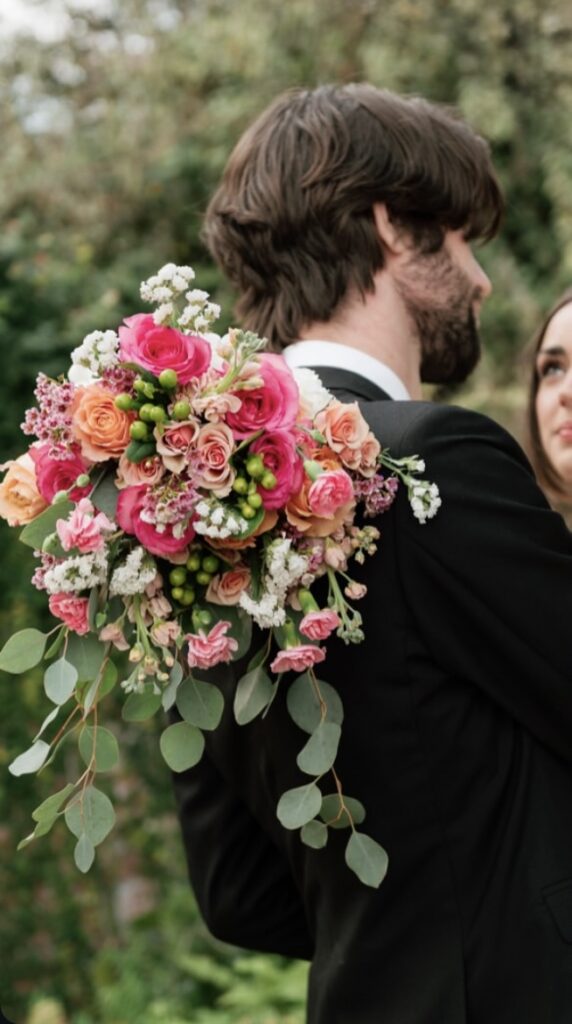 Groom holds romantic pink and green wedding bouquet in garden